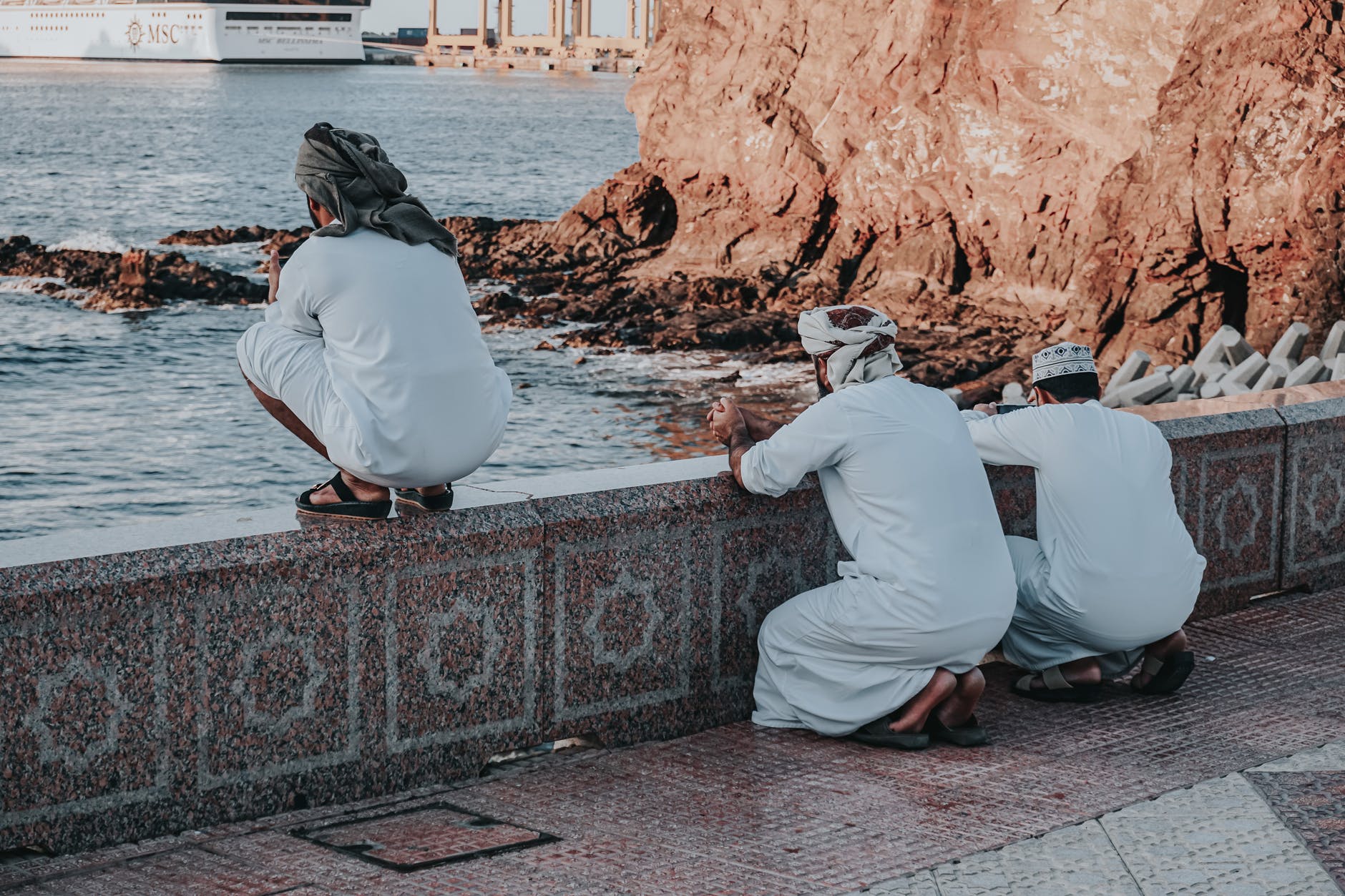 arab men in white traditional wear praying on embankment